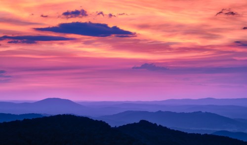 A vibrant sunset paints the sky in shades of pink and purple over rolling mountains and valleys.