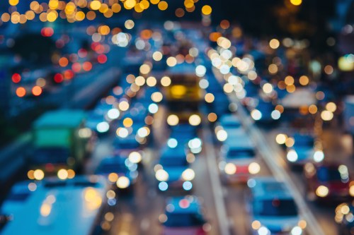 A blurred image of a busy city street at night, filled with colorful lights from vehicles and street lamps.