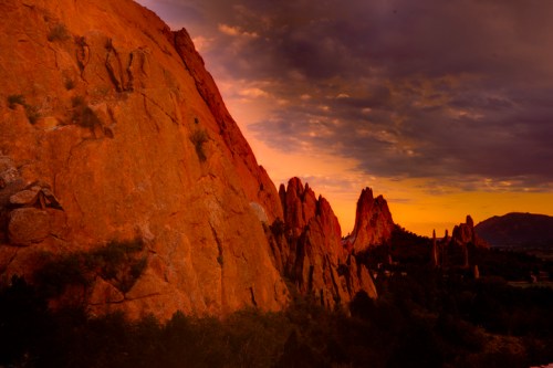 Sunset over rugged rock formations, casting warm hues on the landscape with dramatic clouds in the sky.