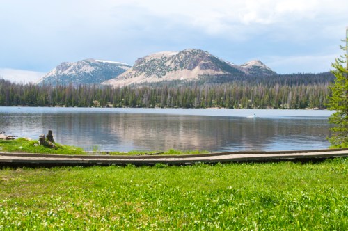 Scenic view of a calm lake surrounded by mountains and lush greenery under a partly cloudy sky.