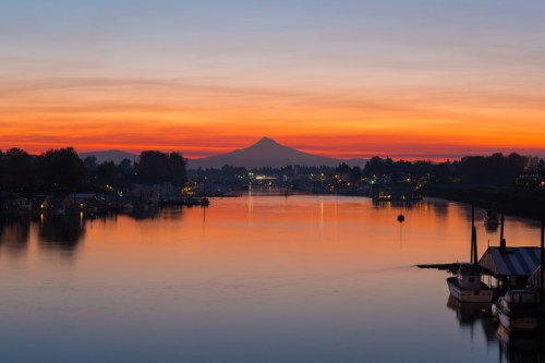 Sunset over a calm river, reflecting vibrant orange and purple hues, with a mountain silhouette in the background.