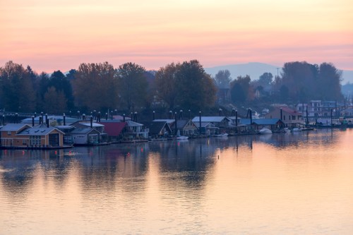 A serene waterfront scene at sunrise, featuring colorful houseboats and calm water reflecting the pastel sky.