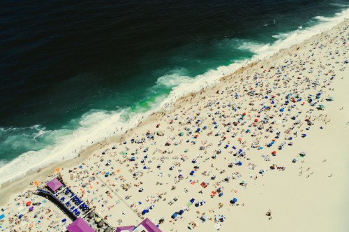 Aerial view of a crowded beach with colorful umbrellas and waves crashing on the shore.