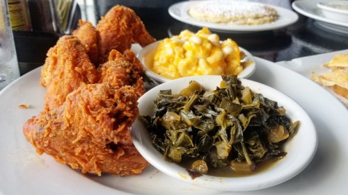 A plate featuring crispy fried chicken, macaroni and cheese, and collard greens.