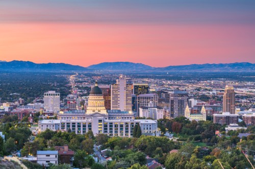 A panoramic view of a city skyline at sunset, featuring buildings and mountains in the background.