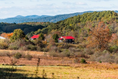 Two cabins with red roofs nestled among colorful autumn trees in a mountainous landscape.
