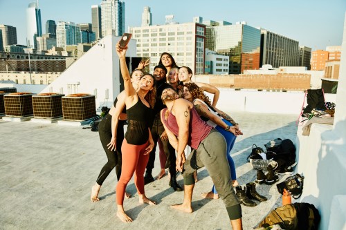 A group of eight people taking a selfie on a rooftop with a city skyline in the background.