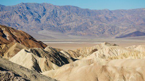A vast desert landscape with layered mountains and hills under a clear blue sky.