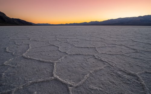 A vast salt flat with hexagonal patterns under a colorful sunset sky and distant mountains.