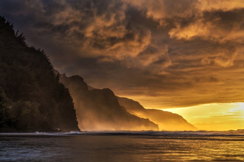 Sunset over a rugged coastline, with dark clouds and mist rising from the ocean, creating a dramatic and serene atmosphere.