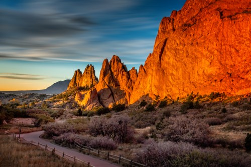 Sunset illuminates towering red rock formations and a winding path in a scenic landscape.