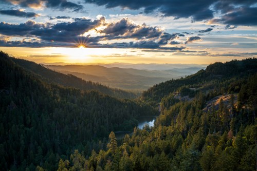Sunset over a lush green valley, with mountains in the distance and a serene lake reflecting the sky.