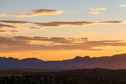 Sunset over a mountain range, with clouds illuminated in warm hues against a fading blue sky.