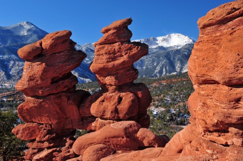 Red rock formations stand against a backdrop of snow-capped mountains and a clear blue sky.