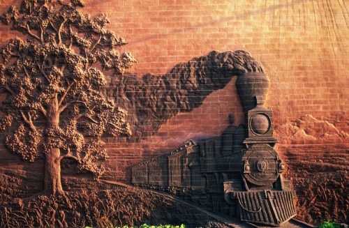 A textured mural depicting a steam train with smoke, surrounded by trees and mountains in the background.