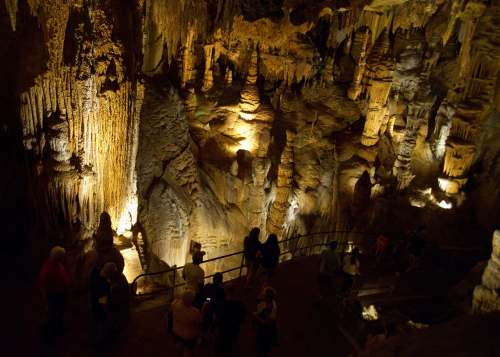 Visitors explore a dimly lit cave filled with illuminated stalactites and stalagmites.