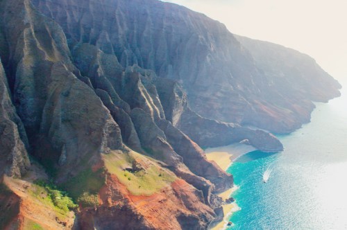 Aerial view of rugged cliffs meeting a turquoise ocean, with a sandy beach nestled between the rocks.