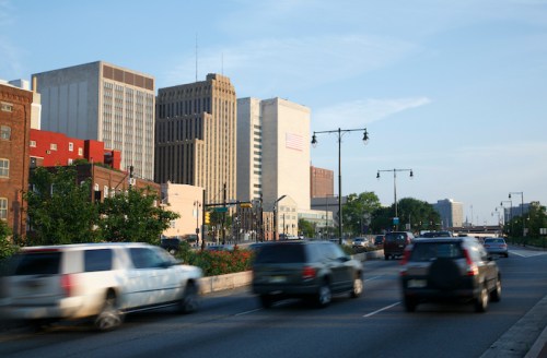 City skyline with tall buildings and cars on a busy road, under a clear blue sky.