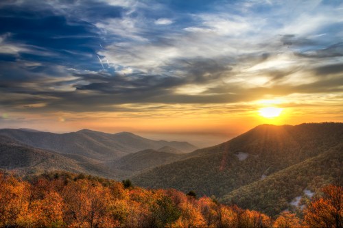 A scenic view of rolling mountains at sunset, with vibrant autumn foliage and a colorful sky.