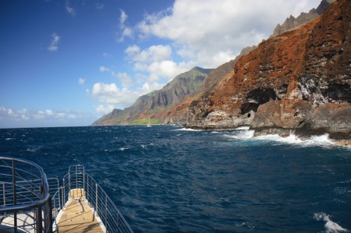 A scenic view of rocky cliffs and turquoise ocean under a partly cloudy sky, with a boat in the foreground.