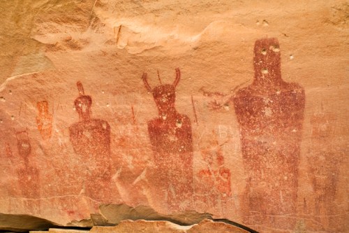 Ancient rock art depicting human figures and symbols on a sandstone surface.