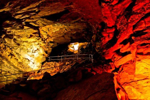 A cave interior with colorful lighting, showcasing rock formations and a staircase leading upward.