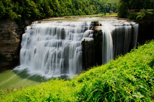 A stunning waterfall cascades over rocky cliffs, surrounded by lush greenery and a serene river below.