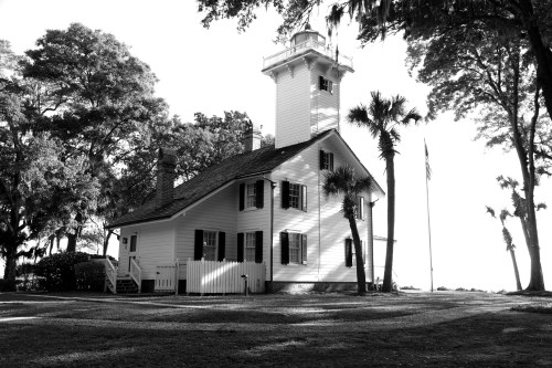 A historic white lighthouse and keeper's house surrounded by trees, captured in black and white.