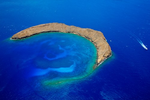 Aerial view of a crescent-shaped island surrounded by vibrant blue ocean waters.