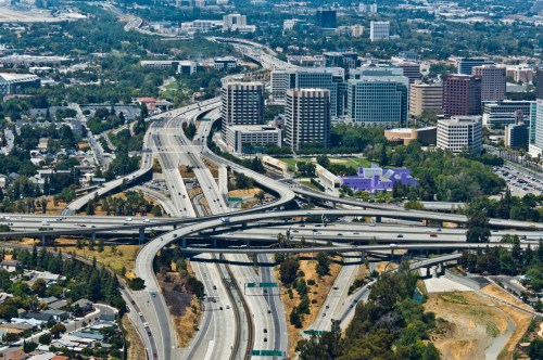 Aerial view of a busy highway interchange surrounded by urban buildings and greenery.