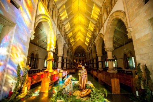 Interior of a church with colorful light reflections, featuring a nativity scene and wooden pews.