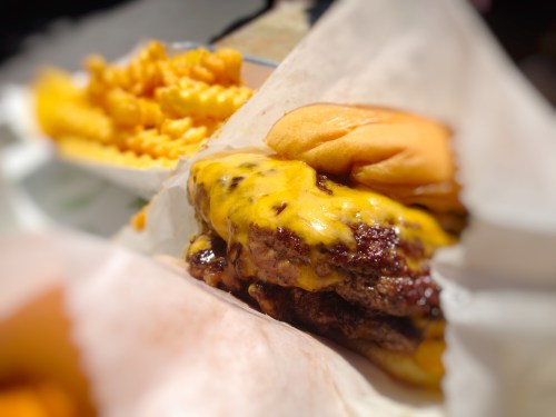 A close-up of a cheeseburger with melted cheese and a side of crinkle-cut fries.
