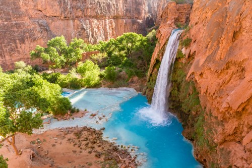 A stunning waterfall cascades into a turquoise pool, surrounded by lush greenery and rocky cliffs.