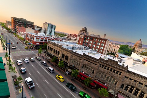 Aerial view of a city street with historic buildings, modern architecture, and cars under a sunset sky.