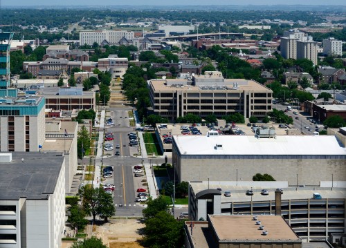 Aerial view of a cityscape featuring buildings, streets, and parking lots under a clear blue sky.