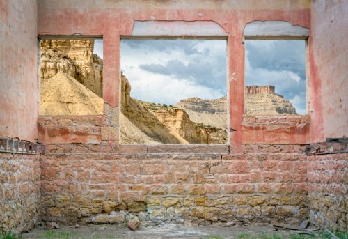 View through three windows of a weathered stone wall, showcasing a dramatic canyon landscape beyond.