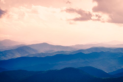 A serene landscape of layered mountains under a cloudy sky, showcasing soft hues and a misty atmosphere.