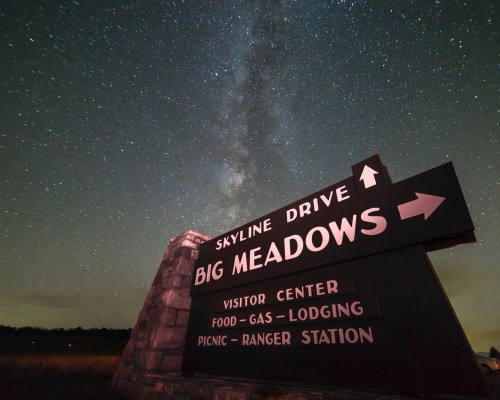 A sign for Skyline Drive and Big Meadows under a starry night sky, with directional arrows and information for visitors.