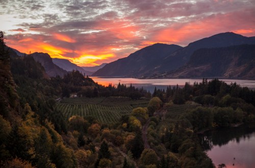 A vibrant sunset over a valley with mountains, a river, and lush vineyards, creating a serene landscape.