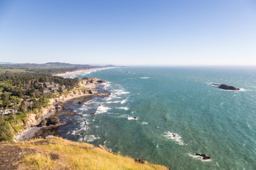 A scenic coastal view with cliffs, a sandy beach, and blue ocean under a clear sky.