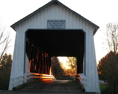 Covered bridge at sunset, with a sign reading "Gallon House Bridge, built in 1916," framed by trees.