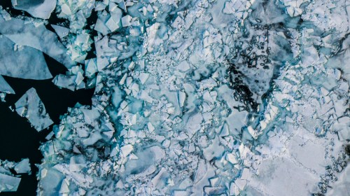 Aerial view of fragmented ice floating on dark water, showcasing a mix of white and blue ice textures.