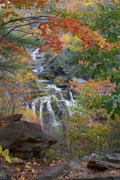 A scenic view of a waterfall surrounded by vibrant autumn foliage in shades of orange, yellow, and green.