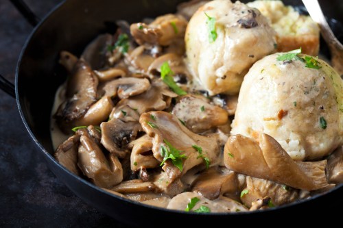 A skillet filled with creamy mushrooms and two dumplings, garnished with fresh herbs.