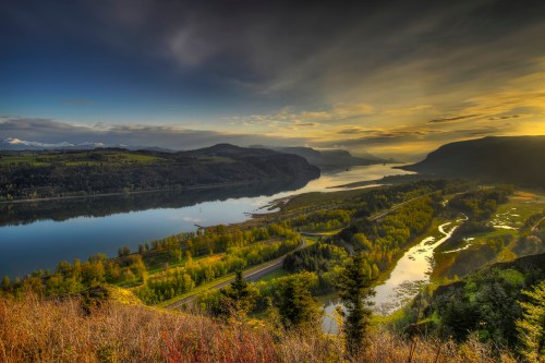A scenic view of a river winding through lush green hills under a dramatic sky at sunset.