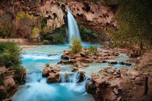 A serene waterfall cascades into turquoise pools, surrounded by rocky terrain and lush greenery.