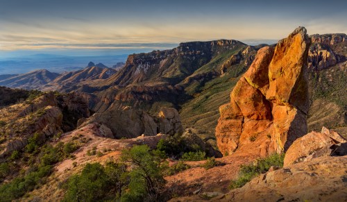 A stunning landscape featuring rugged mountains and vibrant rock formations under a colorful sky.