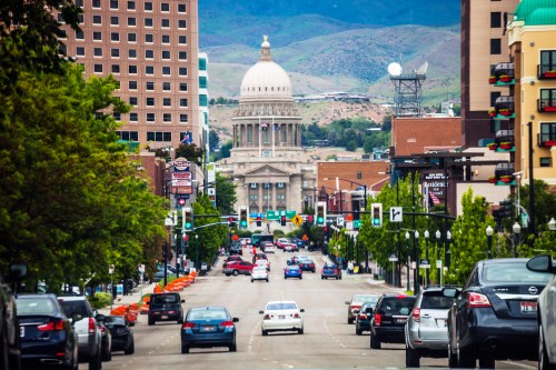 View of a city street lined with trees, leading to a prominent dome building in the background, with cars on the road.