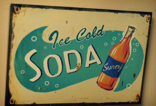 Vintage sign featuring a bottle of soda with the text "Ice Cold Soda" and the word "Sunny" in a playful design.