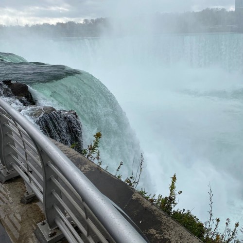 A view of Niagara Falls with rushing water and mist, featuring a railing in the foreground.